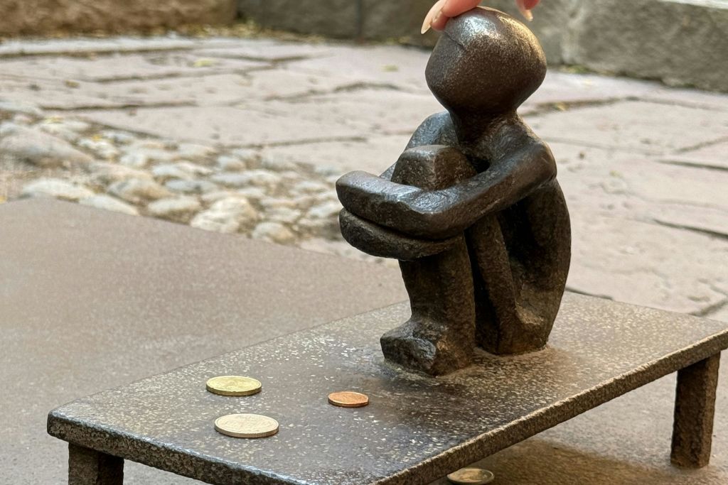 무릎을 감싸고 앉아 있는 사람의 작은 청동 조각상. 동전은 평평한 표면에 앞에 흩어져 있습니다.