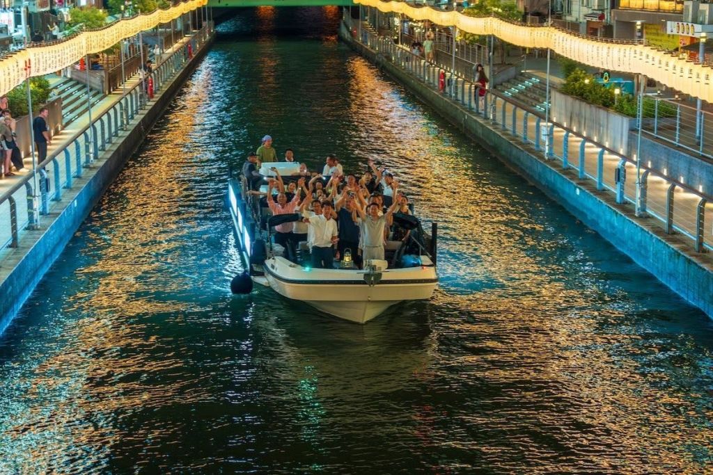 밤에는 강둑에 반짝이는 불빛이 반짝이는 밝은 운하를 따라 사람들이 손을 들고 배를 타고 내려갑니다.