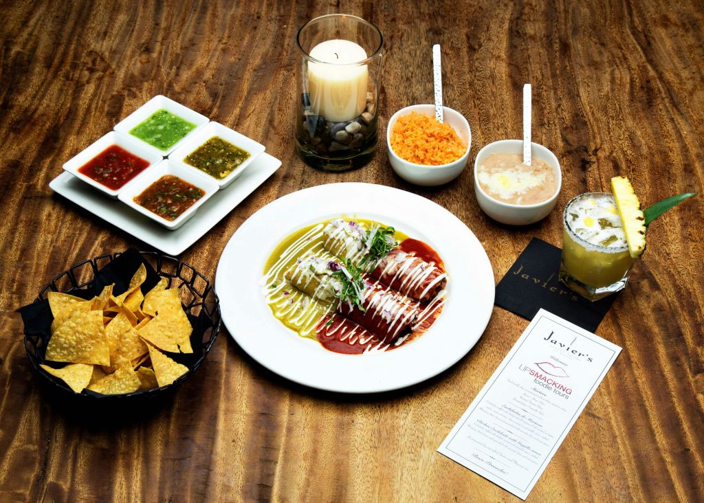 녹색과 빨간색 소스가 담긴 엔칠라다 한 접시, 딥스 칩, 쌀, 콩, 촛불, 나무 테이블에 놓인 음료.