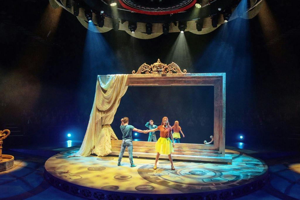 커다란 장식 프레임과 커다란 커튼이 특징인 정교한 조명이 있는 무대에서 공연하는 사람들. 한 가수가 전경에 서 있습니다.