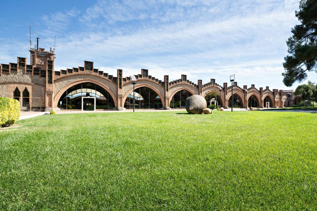 아치형 창문이 있는 벽돌 건물과 앞에 잔디가 깔린 잔디밭, 구름이 흩날리는 푸른 하늘 아래.