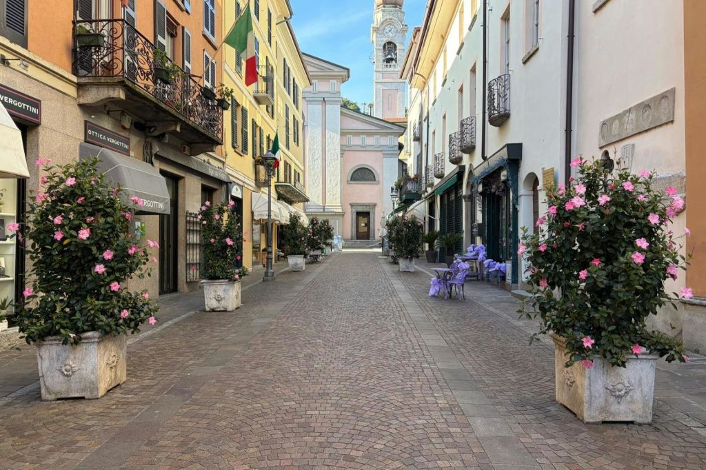 건물과 화분이 늘어선 자갈길은 높은 종탑을 배경으로 한 교회로 이어집니다.