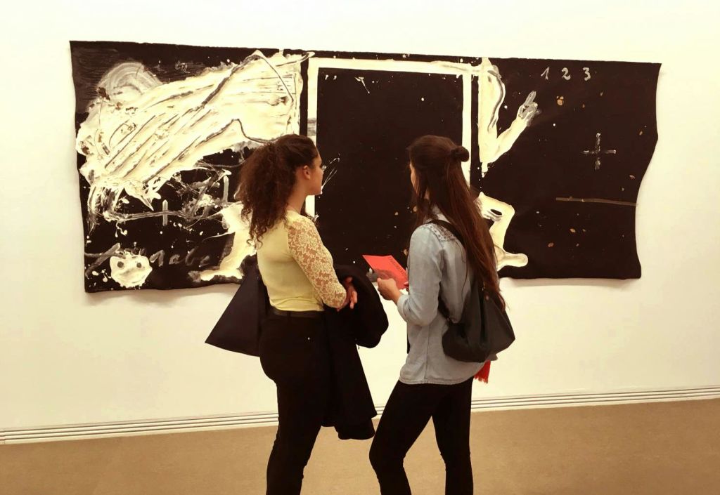 두 명의 여성이 미술관에서 커다란 추상 흑백 그림 앞에 서서 작품에 대해 토론하고 있습니다.