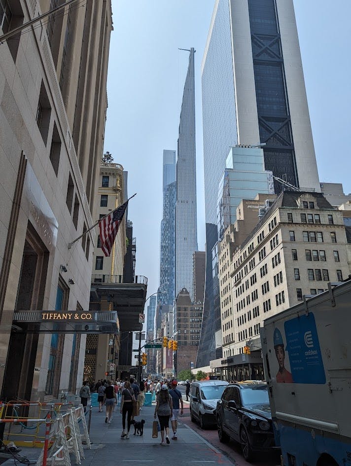 티파니 앤 컴퍼니 (Tiffany & Co.) 를 포함한 높은 건물과 화창한 날 보행자와 차량이 있는 번화한 도시 거리.