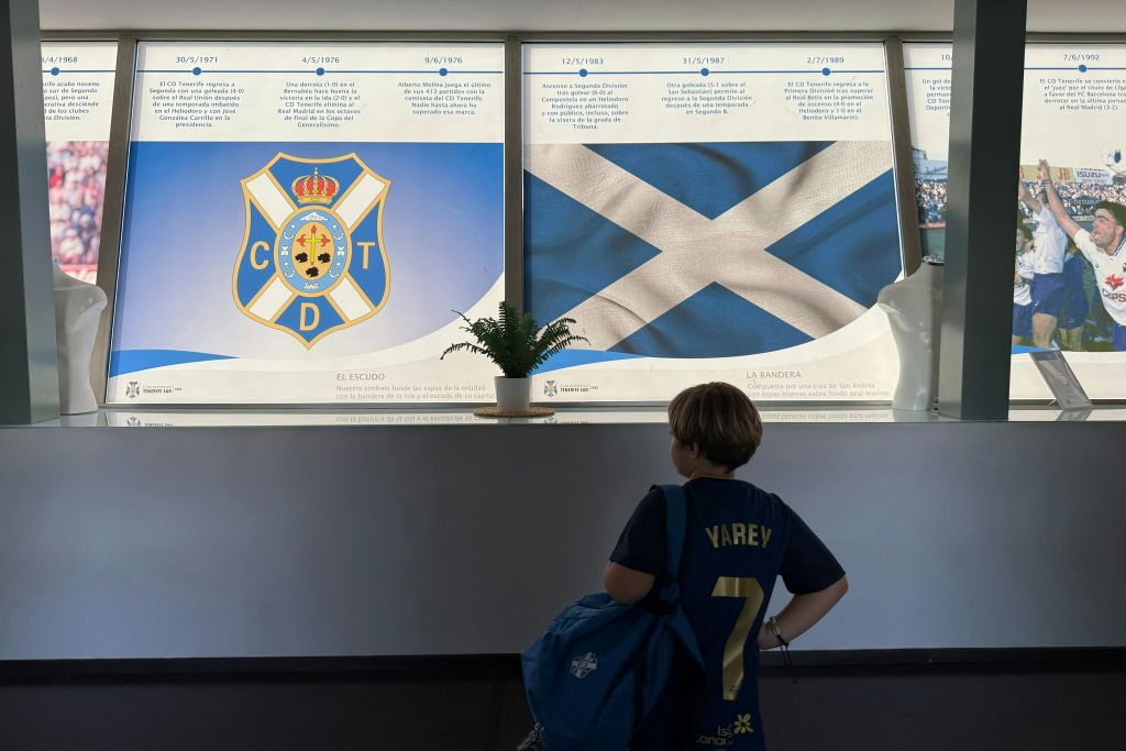 스코틀랜드 국기와 박물관 내부의 안내 포스터가 있는 디스플레이 앞에 스포츠 유니폼을 입은 어린이가 서 있습니다.