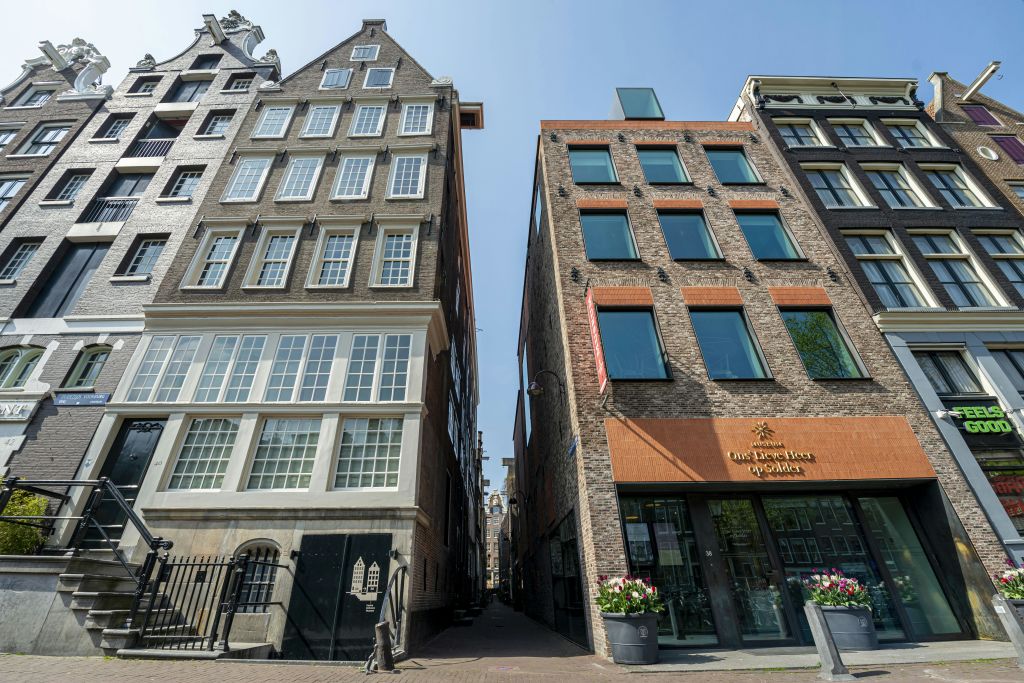 두 개의 높은 건물 사이에 있는 좁은 골목으로, 하나는 창문이 많은 전통 건물이고 다른 하나는 커다란 유리창이 있는 현대 건물입니다.