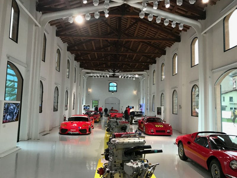 빨간색 자동차와 엔진이 있는 자동차 전시실은 나무 기둥과 아치형 창문이 있는 높은 천장 아래에 전시되어 있습니다.