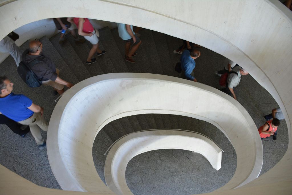 흰색 난간과 어두운 계단이 있는 나선형의 곡선형 계단을 오르내리는 사람들.