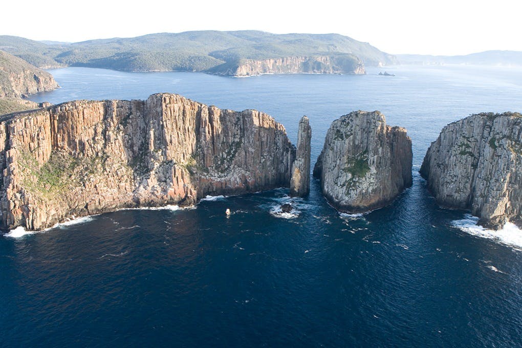 맑은 하늘 아래 먼 언덕이 있는 바다로 둘러싸인 우뚝 솟은 바다 절벽과 바위 지형의 공중 전망.