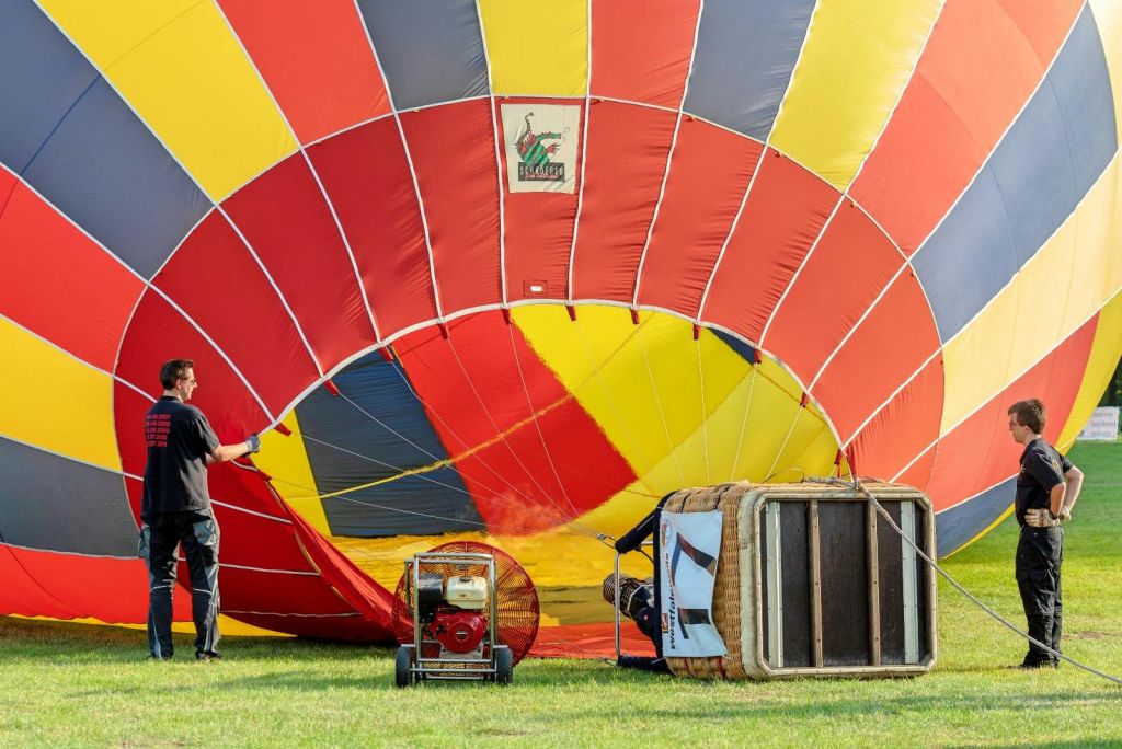 한 사람이 풀밭에서 인플레이션을 위해 화려한 열기구 를 준비합니다. 바구니와 팬이 전면에 있습니다.