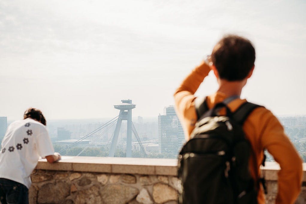 배낭을 메고 석조 발코니에서 미래형 브리지 타워와 도시 풍경을 바라보는 사람.