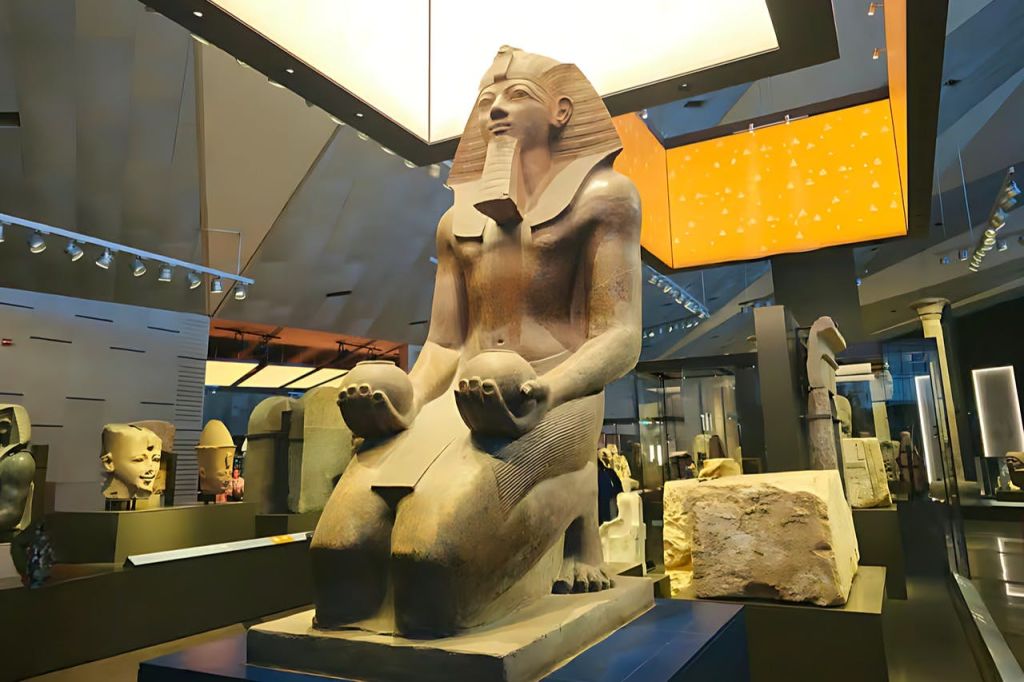파라오가 무릎을 꿇고 구형 물건을 들고 있는 커다란 고대 이집트 조각상이 현대 미술관에 전시되어 있습니다.