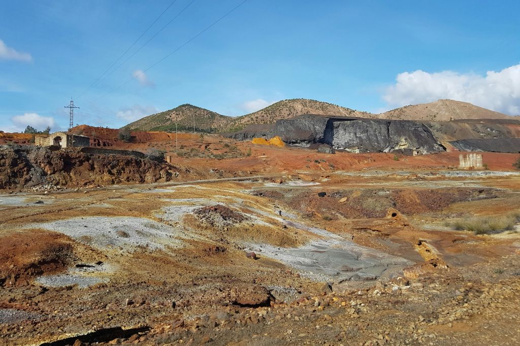 여러 가지 빛깔의 대지와 푸른 하늘 아래 흩어져 있는 구름이 있는 먼 언덕이 있는 황량하고 바위 같은 풍경.