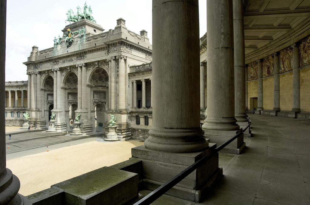 동상으로 장식된 역사적인 건물이 있는 안뜰로 이어지는 전경에 커다란 기둥이 있는 석조 아치길.