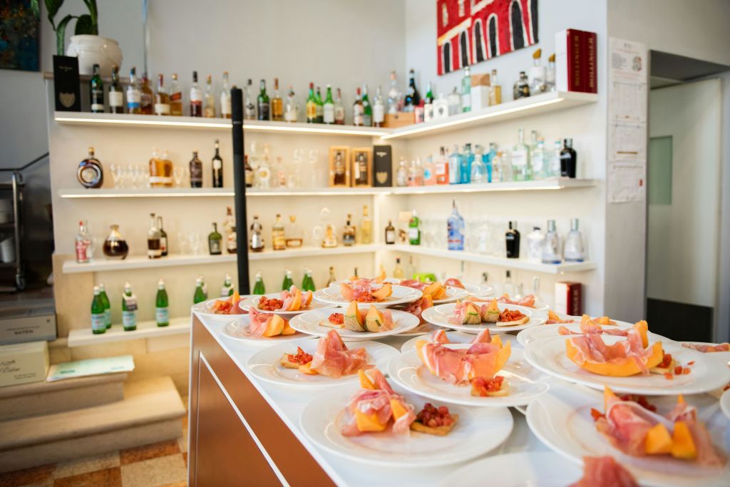 다양한 병으로 가득 찬 선반과 얇게 썬 고기와 멜론을 카운터에 놓은 애피타이저 접시가 있는 바입니다.