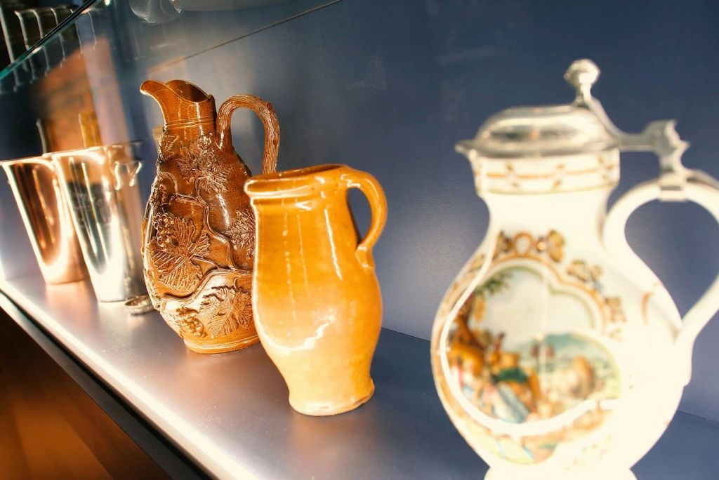 세 개의 세라믹 주전자가 선반에 전시되어 있으며, 하나는 정교하게 조각된 것이고, 다른 하나는 평범한 오렌지색이며, 다른 하나는 디테일한 디자인으로 칠해진 것입니다.
