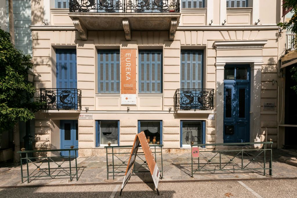 파란색 셔터, 발코니, '유레카' 라고 적힌 표지판이 있는 베이지색 건물입니다. A자형 도로 표지판.