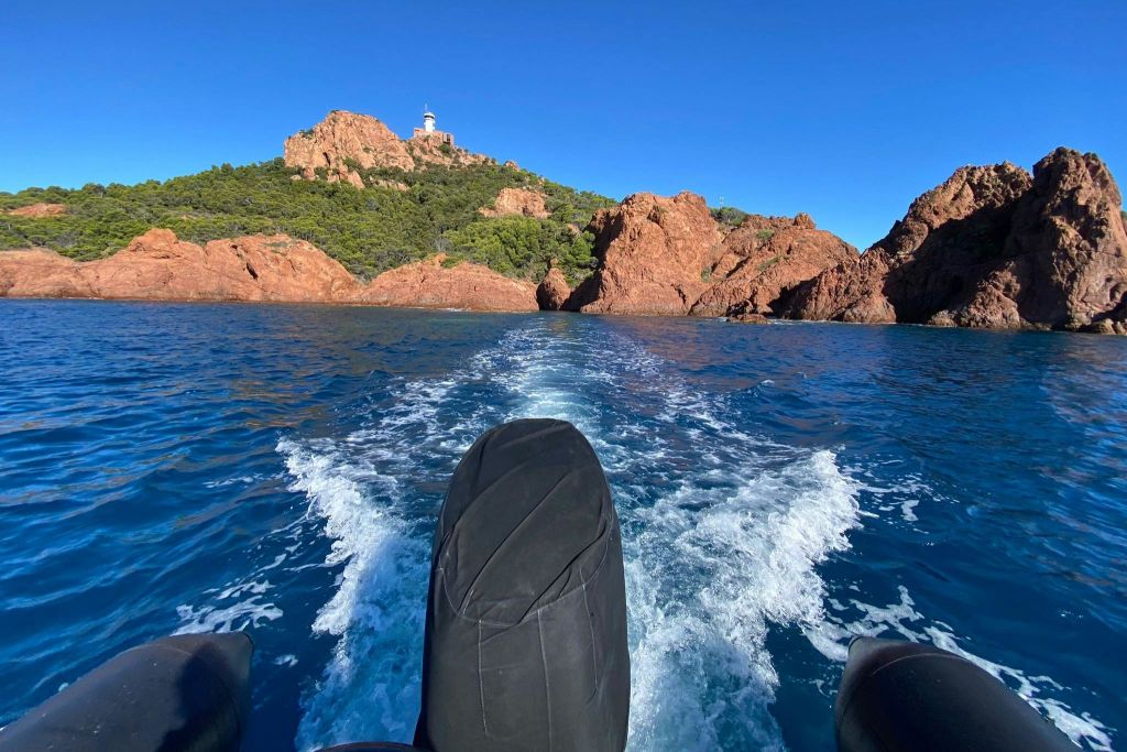 맑고 푸른 하늘 아래 언덕 꼭대기에 등대가 있는 바위 해안선을 보여주는 보트에서 바라보는 풍경.