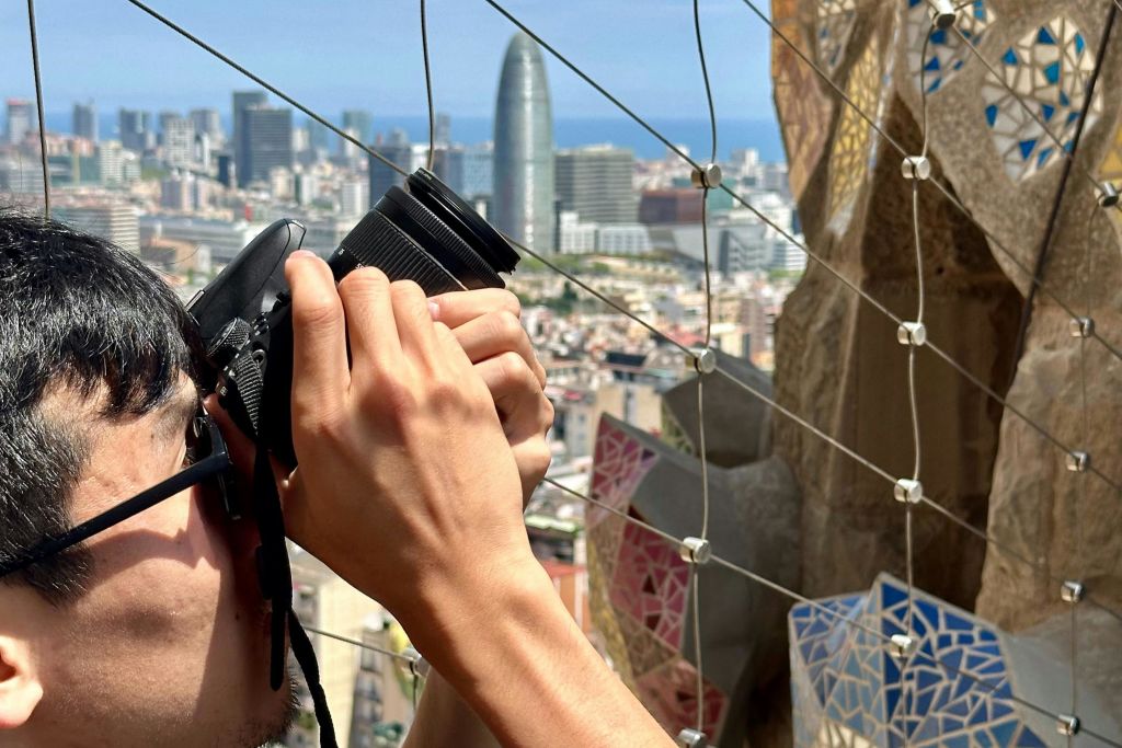 카메라를 들고 높은 건물과 독특한 원통형 마천루를 배경으로 도시의 스카이라인을 촬영하는 사람.