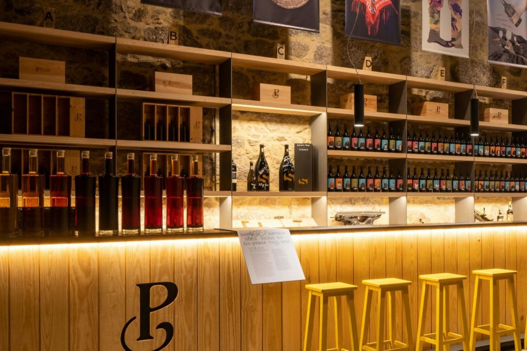 와인 병, 노란색 스툴이 있는 백라이트 카운터, 따뜻한 인테리어가 돋보이는 목재 선반이 있는 세련된 바입니다.