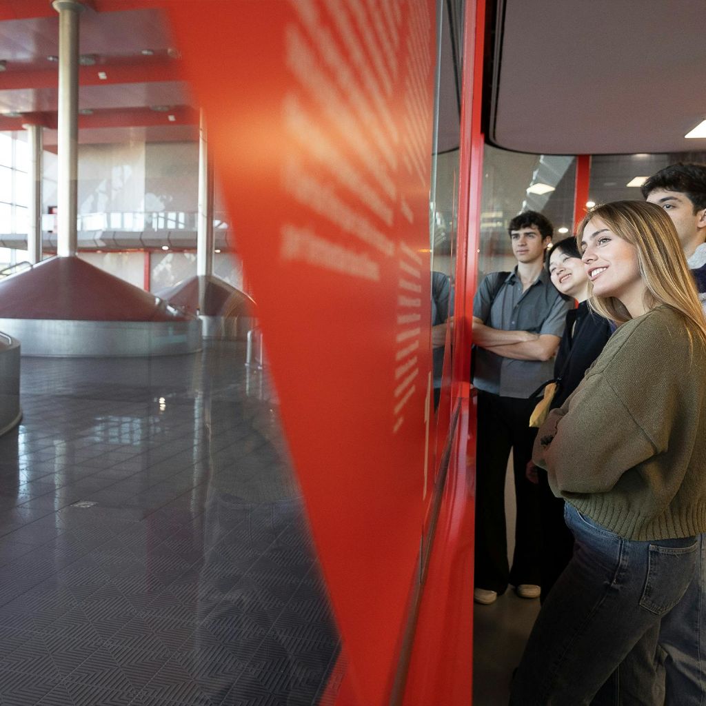 현대적이고 넓은 산업 환경에서 붉은 장벽 뒤의 전시물을 관찰하는 젊은 성인 그룹.