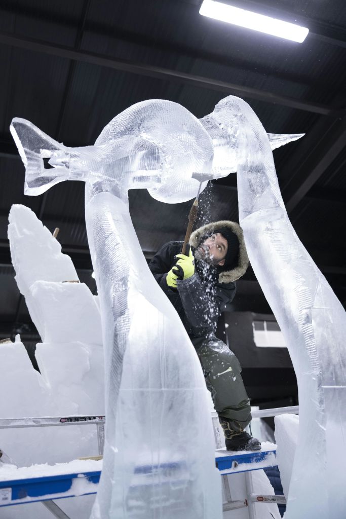 면류관과 세밀한 날개를 가진 날개 달린 사람 얼굴 생물을 향해 손짓하는 사람의 조명된 얼음 조각.