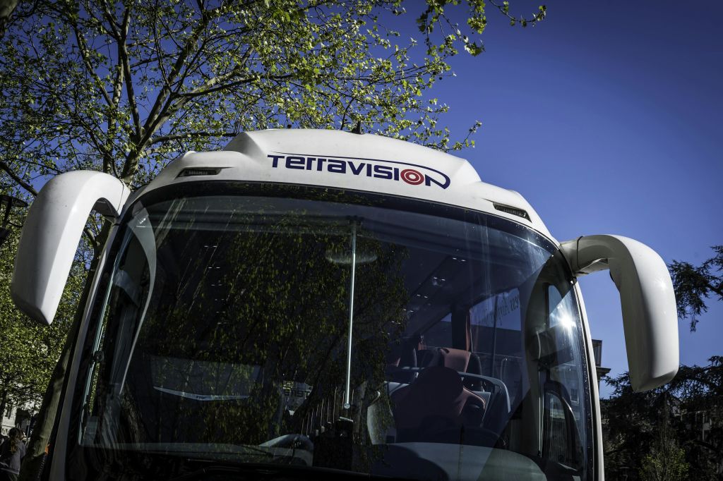 푸른 잎이 우거진 나무 아래 테라비전 버스의 정면도. 배경에는 맑고 푸른 하늘이 있습니다.
