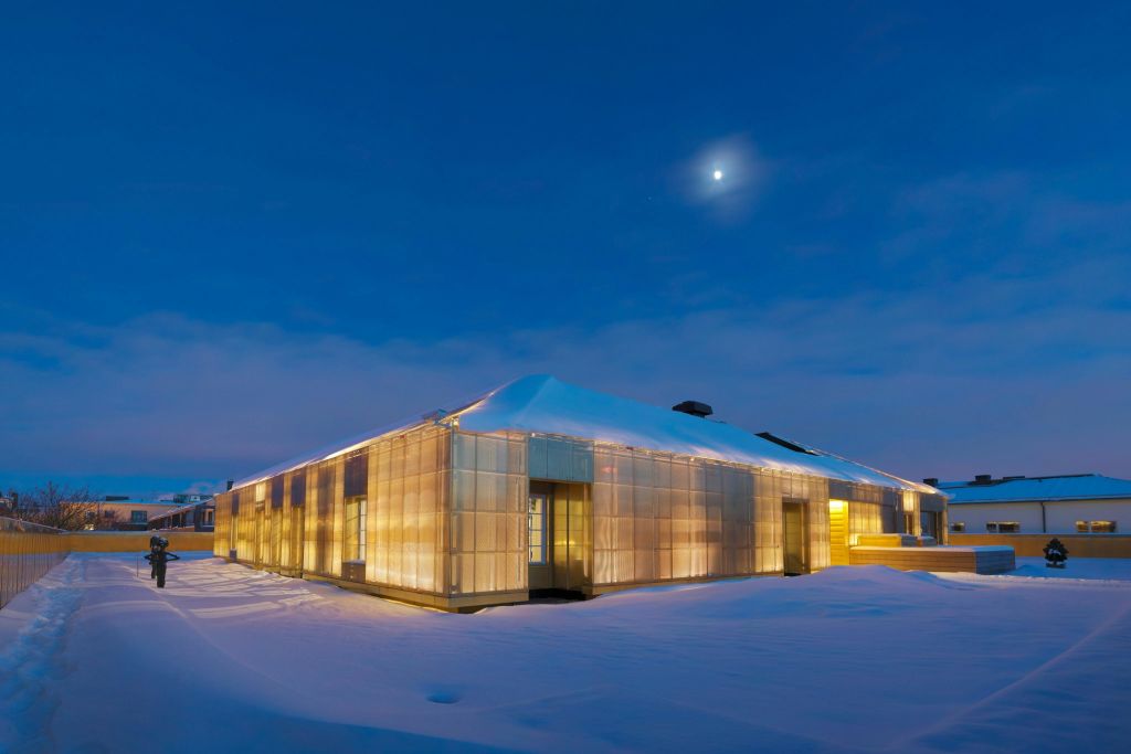 달빛이 비추는 하늘 아래 해질녘 눈 덮인 풍경에 조명이 켜진 현대적인 건물이 서 있습니다.