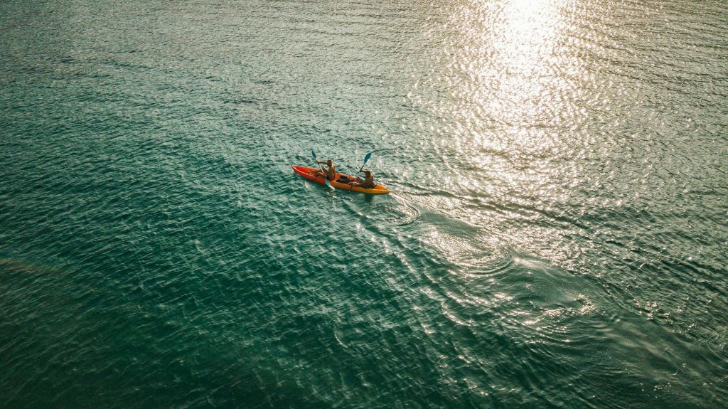 햇살이 내리쬐는 잔잔한 바다에서 카약을 타는 두 사람.