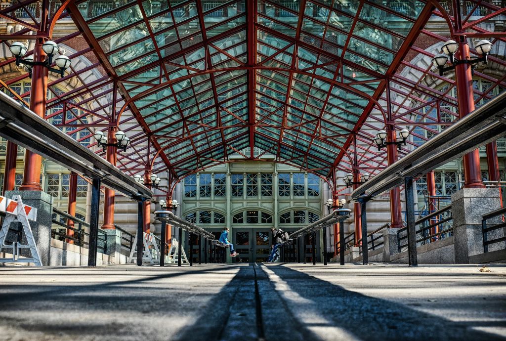 커다란 창문과 사람들이 걸어다니는 웅장한 입구로 이어지는 산책로를 덮고 있는 화려한 유리와 붉은 금속 캐노피.