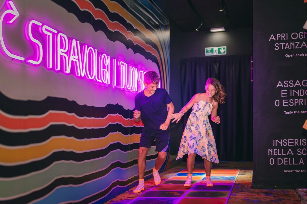 뒤쪽 벽에 네온 불빛과 이탈리아 문자가 있는 화려한 조명 바닥에서 한 남녀가 춤을 추고 있습니다.