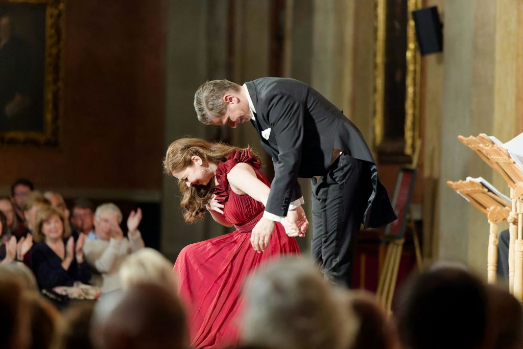 정장 차림의 두 사람이 무대에서 활을 쏘고 관객은 풍성하게 꾸며진 실내에서 박수 갈채를 보냅니다.