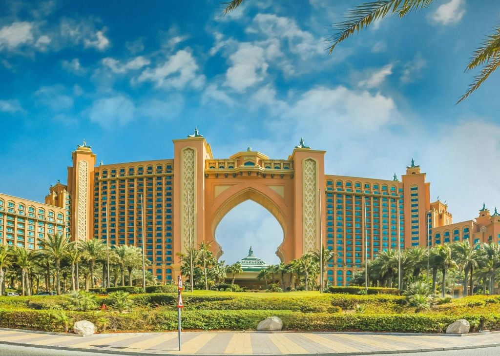 부분적으로 흐린 하늘 아래 야자수와 울창한 조경으로 둘러싸인 중앙에 아치형 통로가 있는 크고 고급스러운 호텔입니다.