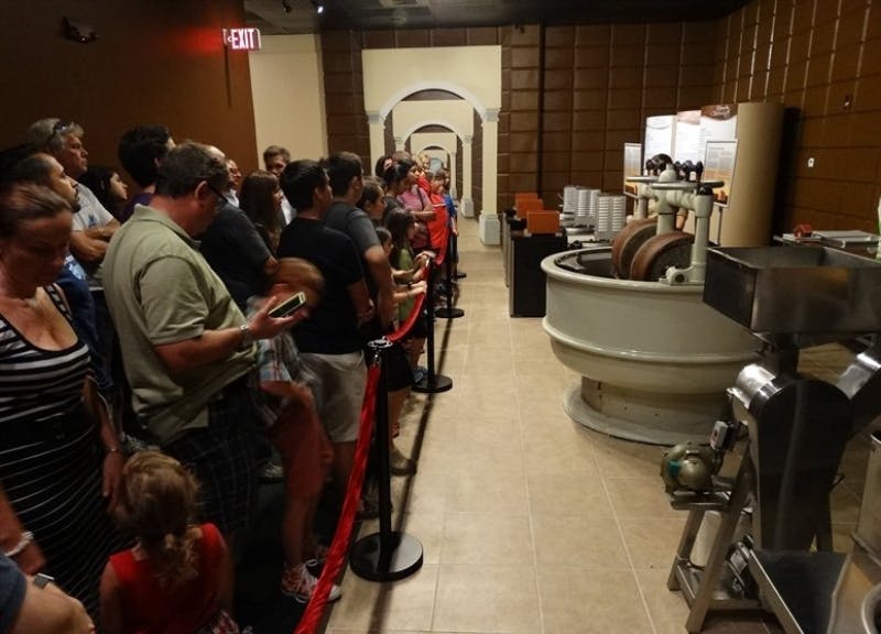 전시실 내부에 줄을 서서 근처에 정보 디스플레이가 있는 크고 둥근 산업용 기계를 관찰하는 사람들.