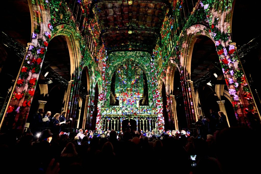 활기찬 꽃무늬가 투영된 교회 내부에는 많은 사람들이 모여 전시를 지켜보고 있습니다.