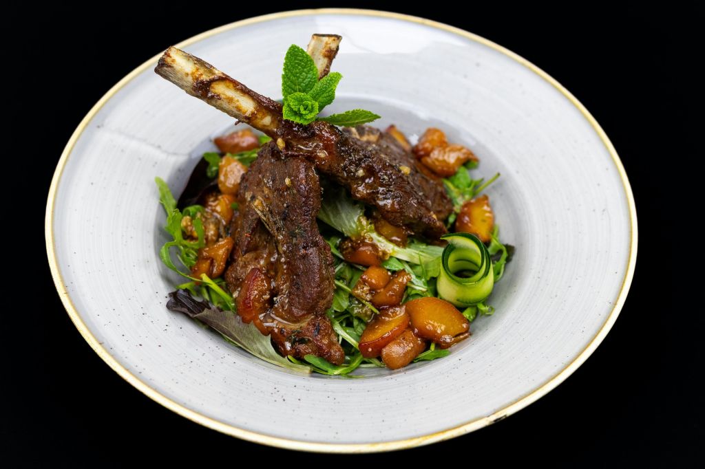 깍뚝썰기한 야채, 민트 잎, 오이 컬로 장식한 신선한 채소를 곁들인 양갈비 구이 도금 요리입니다.