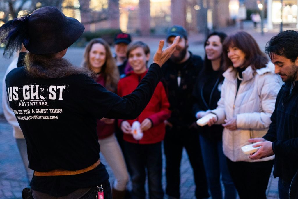 Tour guide making a tour group laugh while they hold EMF detectors, picking up on spiritual activity