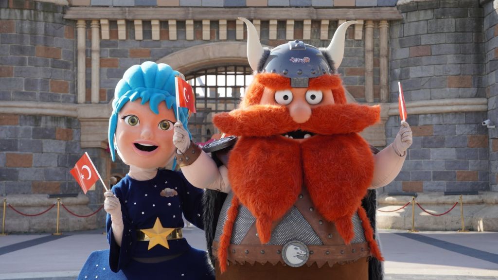 파란색 머리카락과 바이킹 복장을 한 의상을 입은 두 명의 캐릭터가 석조 건물 앞에 터키 국기를 들고 있습니다.