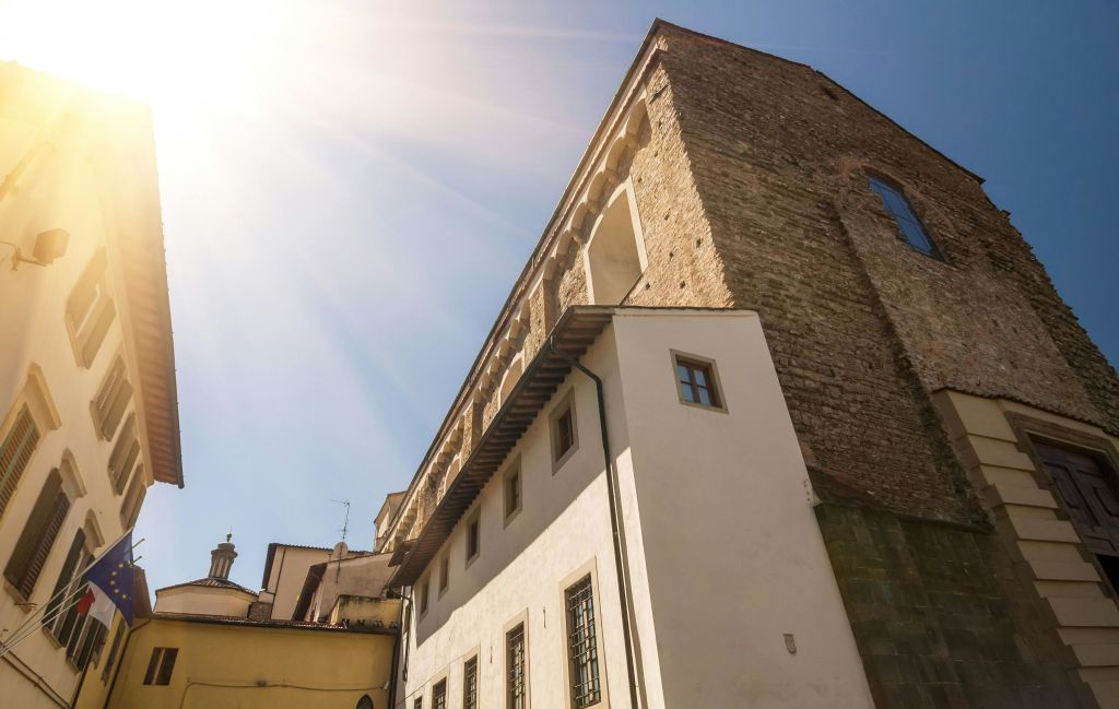 맑고 푸른 하늘 아래 아치형 창문이 있는 역사적인 돌과 치장 벽토 건물 위로 햇살이 비치고 있습니다.