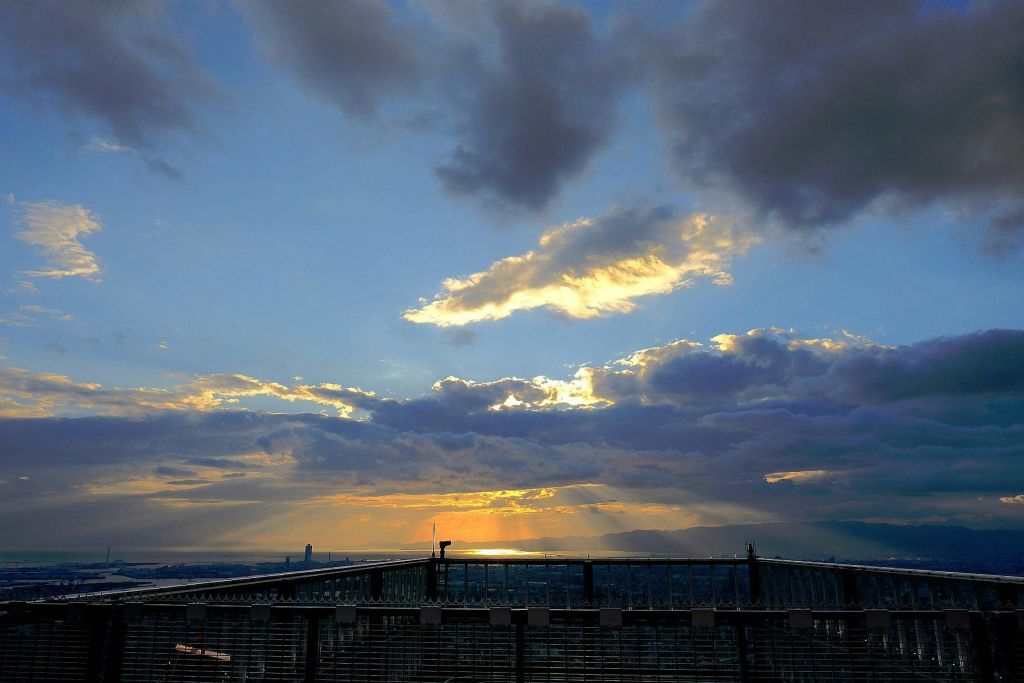 저 멀리 도시의 스카이라인이 내려다보이는 탁 트인 구름과 태양 광선이 어우러진 옥상에서 바라보는 석양.