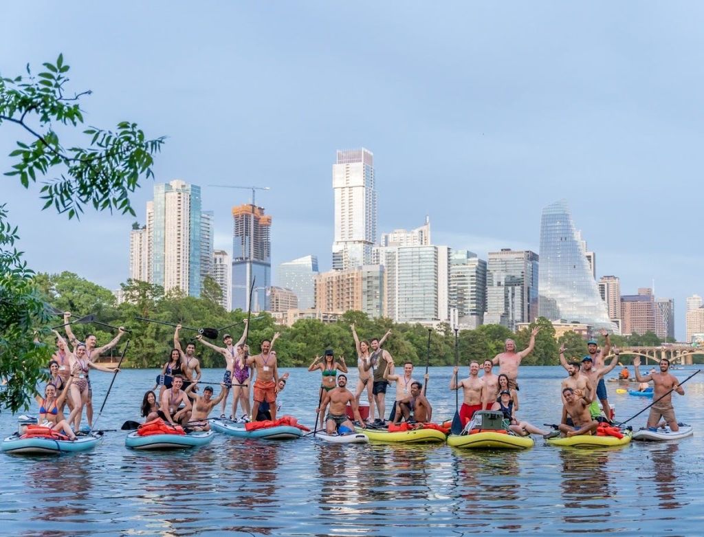 도시의 스카이라인과 녹지를 배경으로 호수에서 패들보드를 타는 사람들.