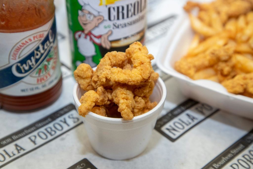 뜨거운 소스 한 병 옆에 튀긴 음식이 가득 담긴 하얀 컵과 테이블 위에 놓인 조미료 용기.