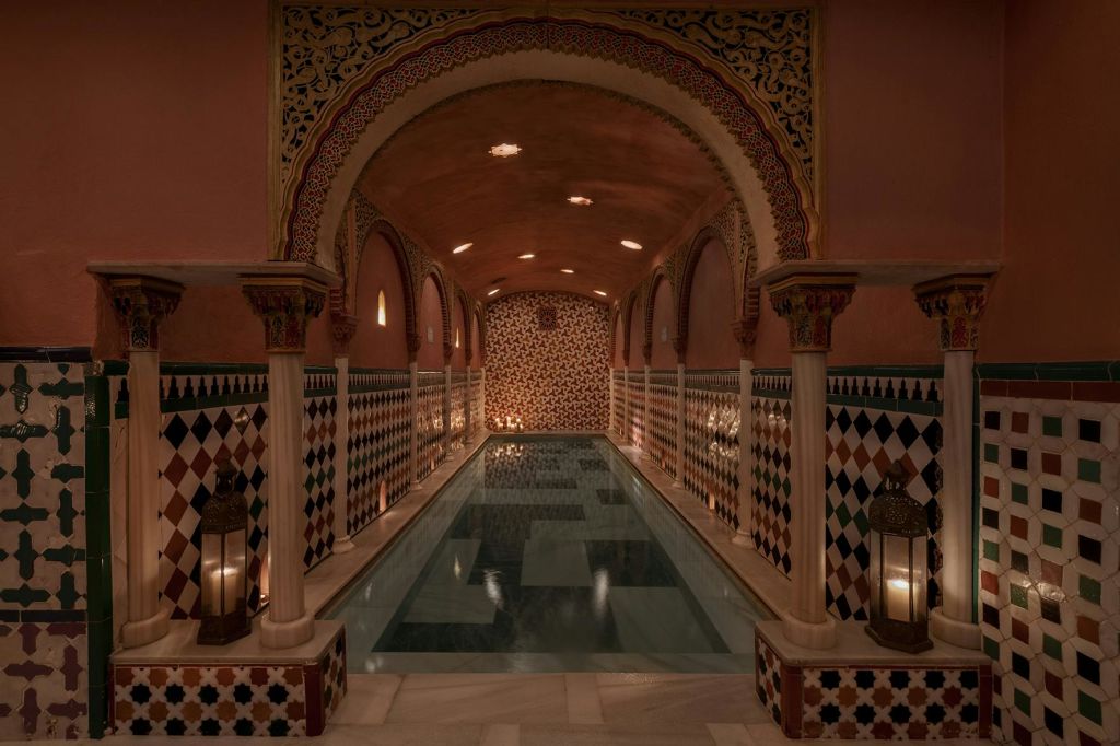타일 벽, 아치형 통로, 기둥, 랜턴이 있는 화려한 실내 수영장은 따뜻하고 매력적인 분위기를 연출합니다.