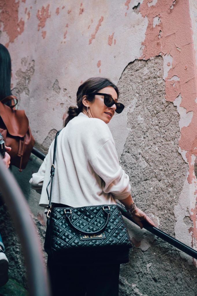 선글라스와 흰색 셔츠를 착용한 여성이 질감이 살짝 벗겨진 벽 옆 계단을 오르며 뒤를 돌아보고 있습니다.