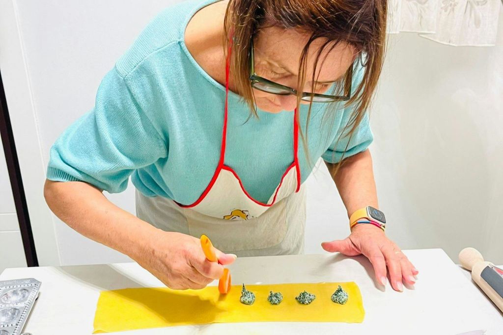 파란색 상단과 앞치마를 입은 사람은 녹색 충전재로 반죽을 준비하기 위해 브러시를 사용합니다. 아마도 파스타나 라비올리를 만들 것입니다.