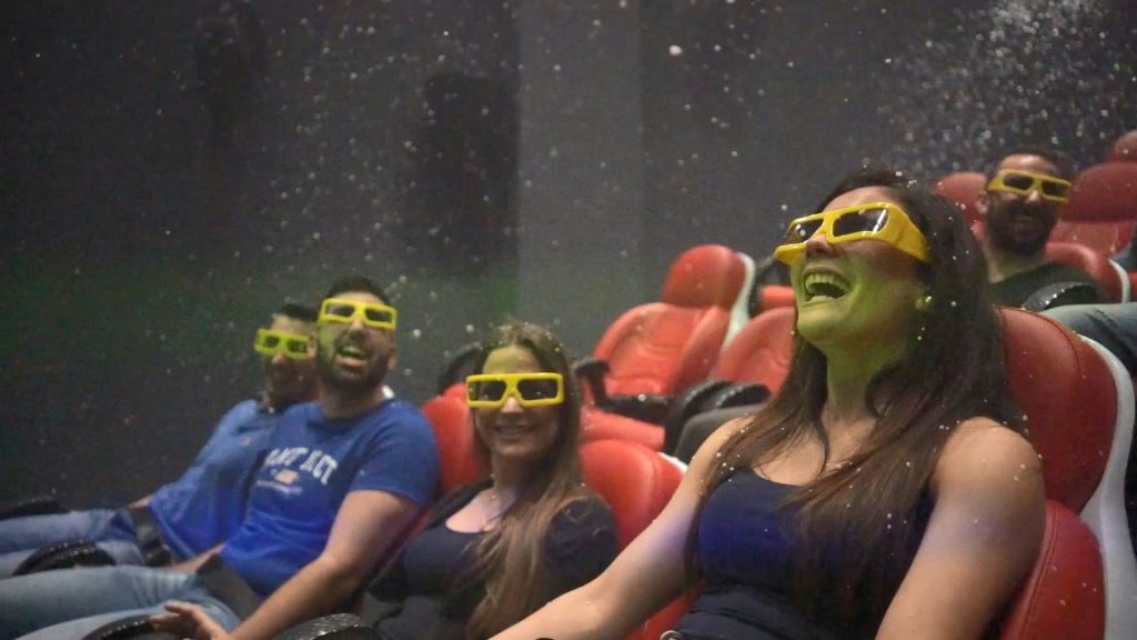 노란색 3D 안경을 쓴 미소 짓는 사람 세 명이 빨간색 극장 좌석에 앉아 있으며, 눈 같은 입자가 눈 주위를 감싸고 있습니다.