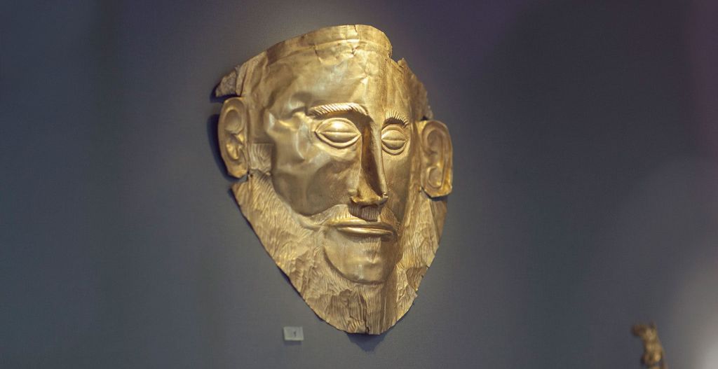 어두운 벽에 표시되는 상세한 얼굴 특징이 있는 고대 금 장례식 마스크입니다.