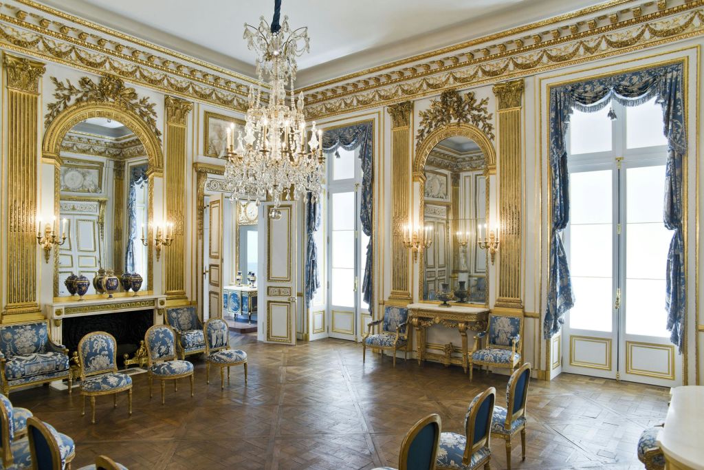 골드 테두리가 있는 화려한 객실, 커다란 샹들리에, 파란색과 금색으로 덮인 의자, 정교한 디테일이 돋보이는 거울 벽 패널.