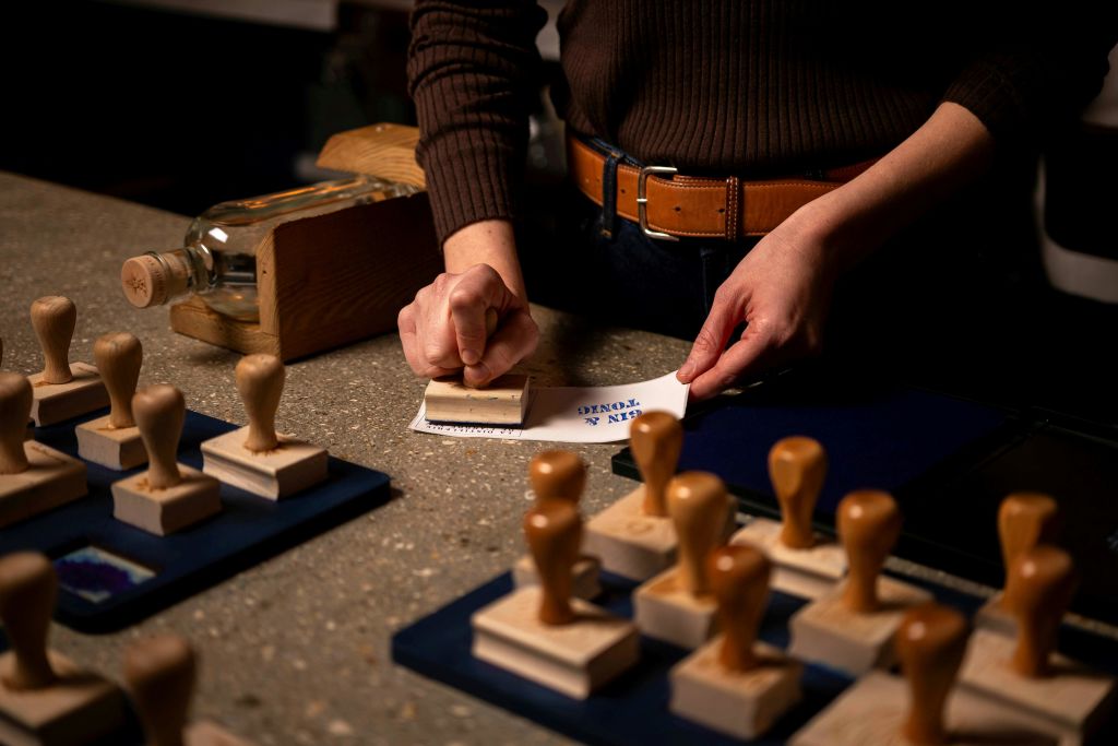 조명이 어두운 테이블에 여러 개의 나무 스탬프와 스테이플러가 있는 종이에 스탬프를 누르고 있는 사람.
