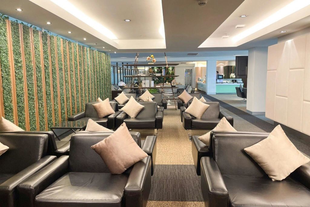 따뜻한 천장 조명 아래 검은색 안락의자, 베이지색 쿠션, 장식용 식물이 있는 현대적인 라운지 공간입니다.